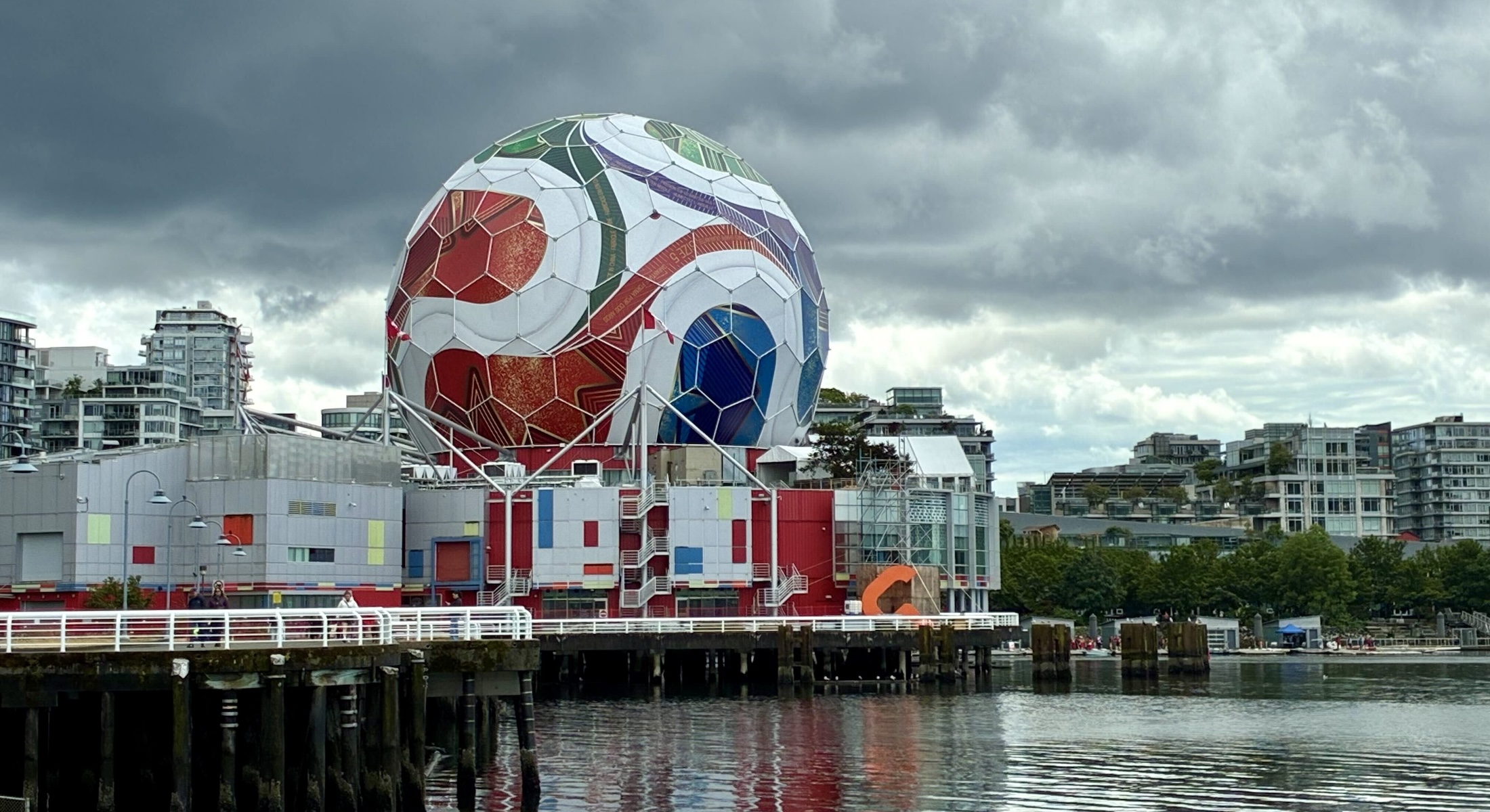 A view from across the water of Science World in Vancouver, an orb-shaped structure covered in material that resembles a colourful FIFA World Cup soccer ball.