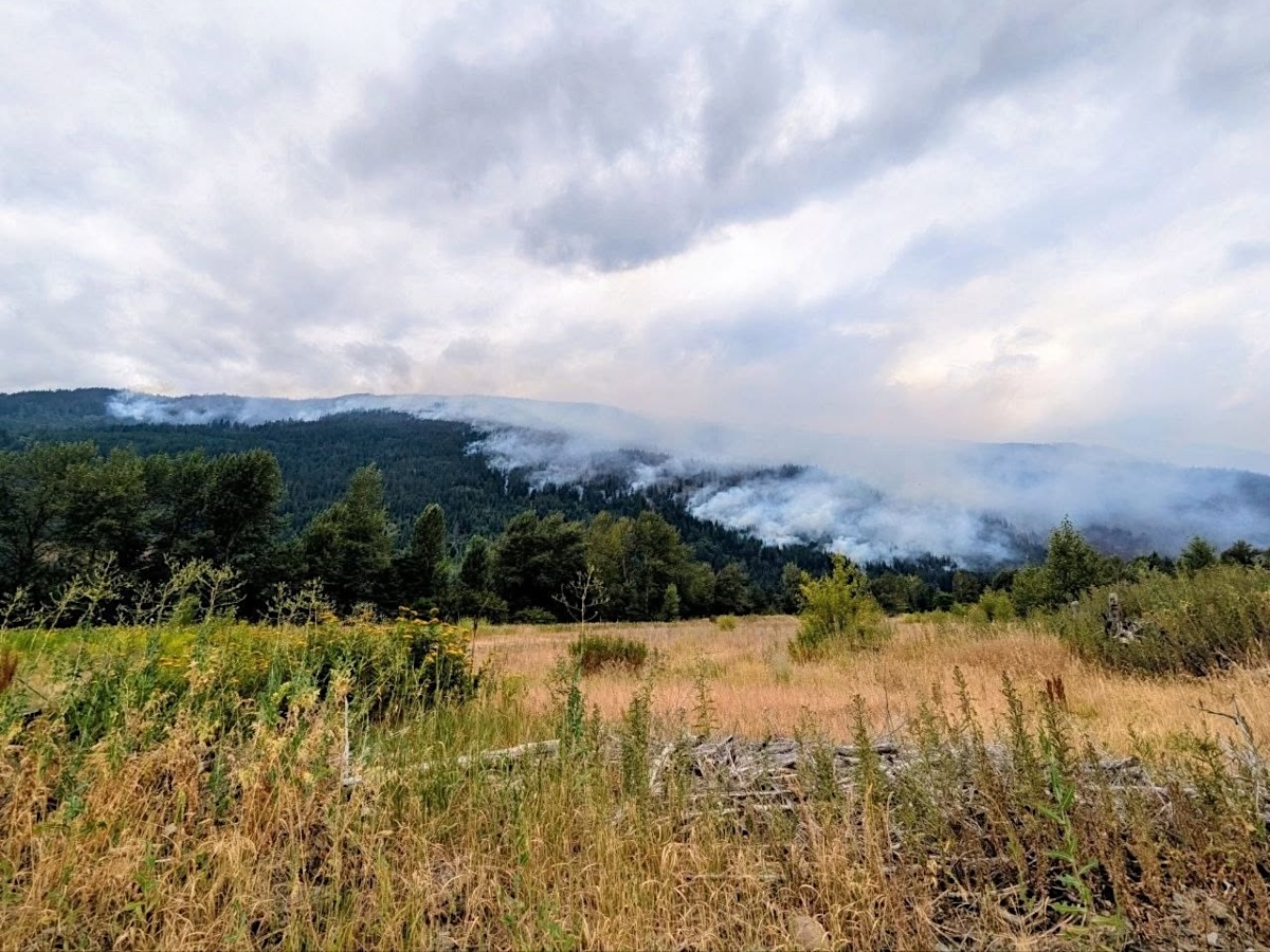 Smoke blows across a broad mountainside in front of a grassy field.