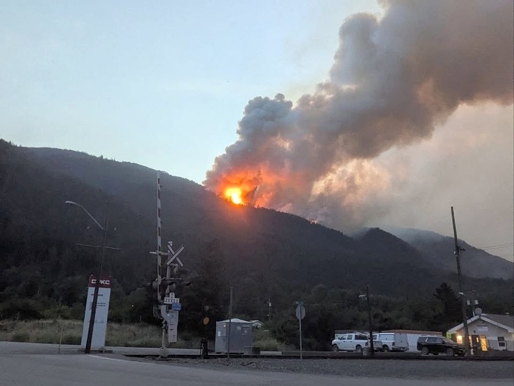 Flames are visible on a hillside above a rail crossing.