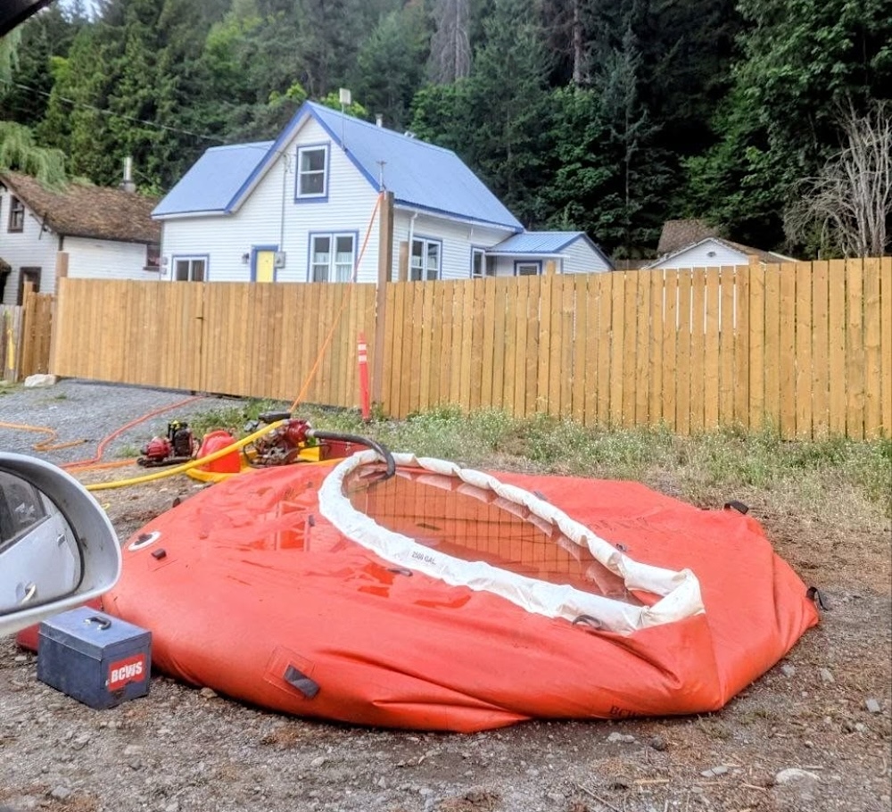 A hose fills a large flexible orange water container that vaguely resembles an above-ground pool.