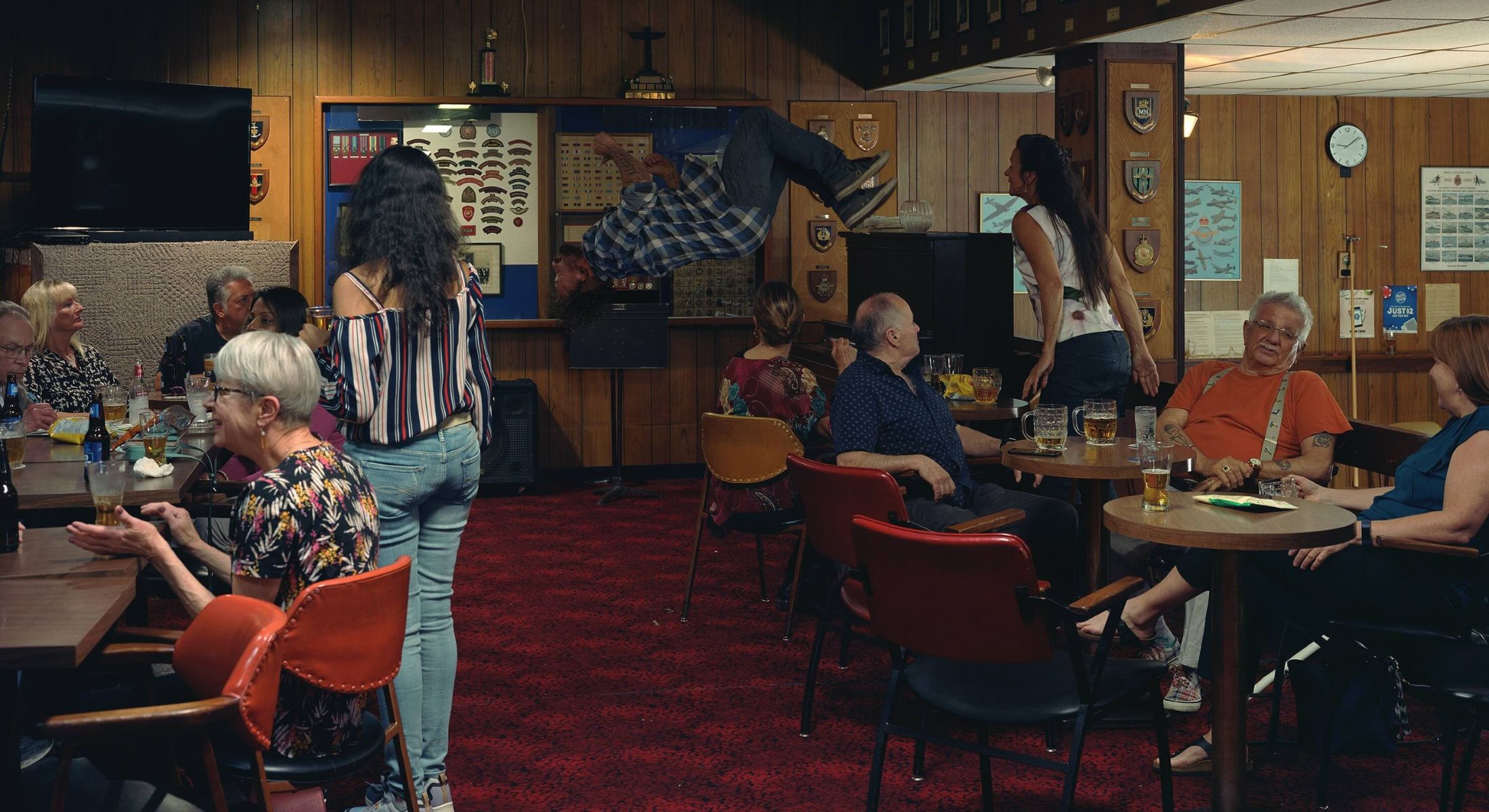 Jeff Wall&rsquo;s In the Legion is a conceptual photograph that depicts the dimly lit interior of a legion hall where people are drinking beer and socializing. In the background a man is doing a backflip.