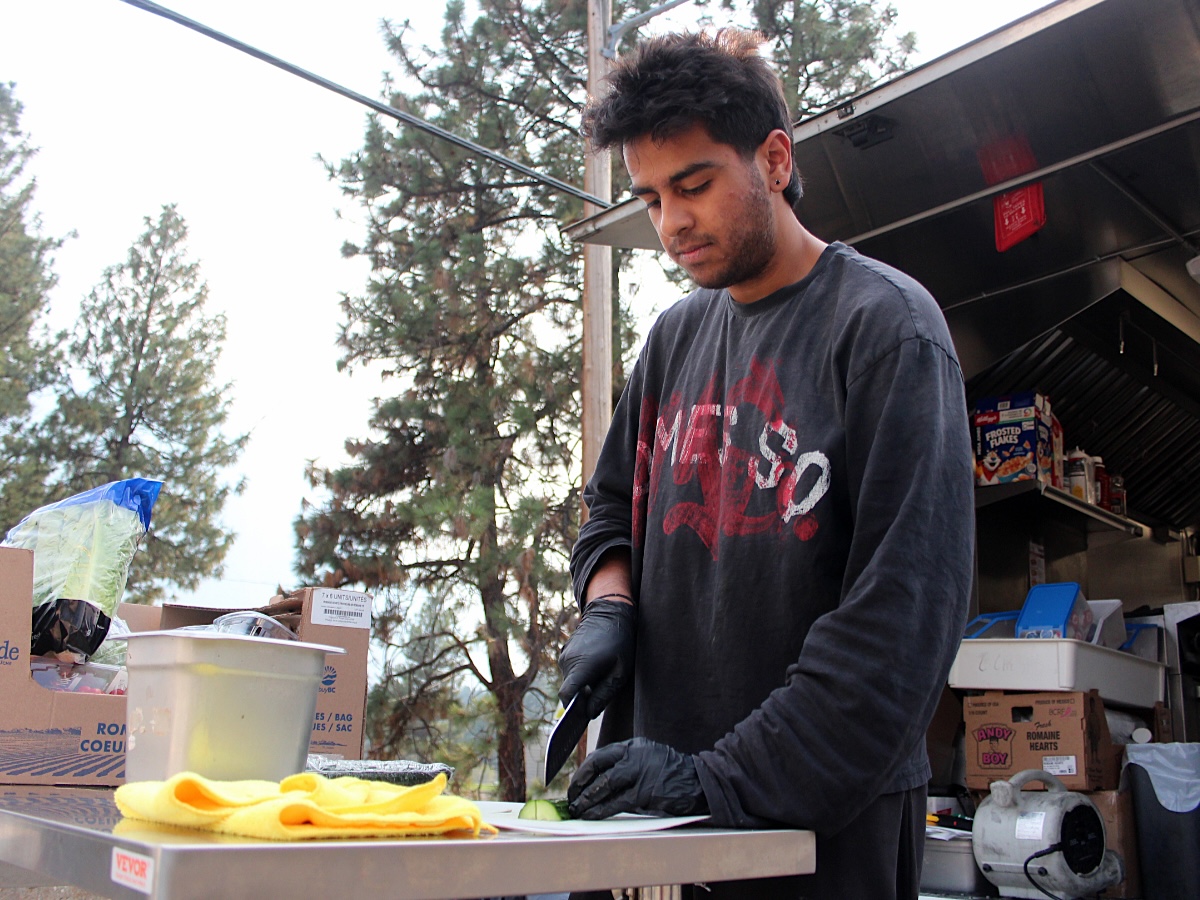 A young man chops a cucumber on a table placed outside.