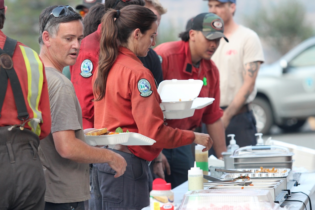 Male and female firefighters line up for a catered meal and scoop food into cardboard containers.