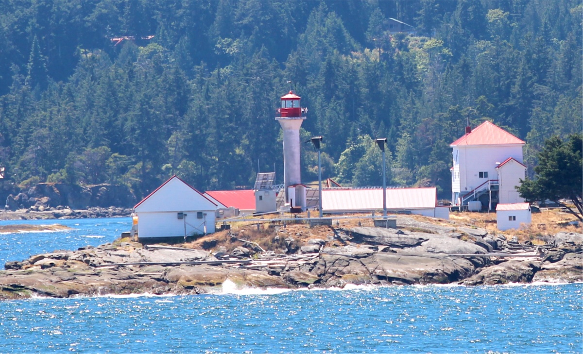 The Entrance Island lighthouse with a Vancouver Island landscape of trees and mountains behind it. 