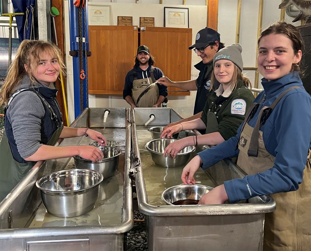 People line up along long metal sinks with stainless steel bowls.