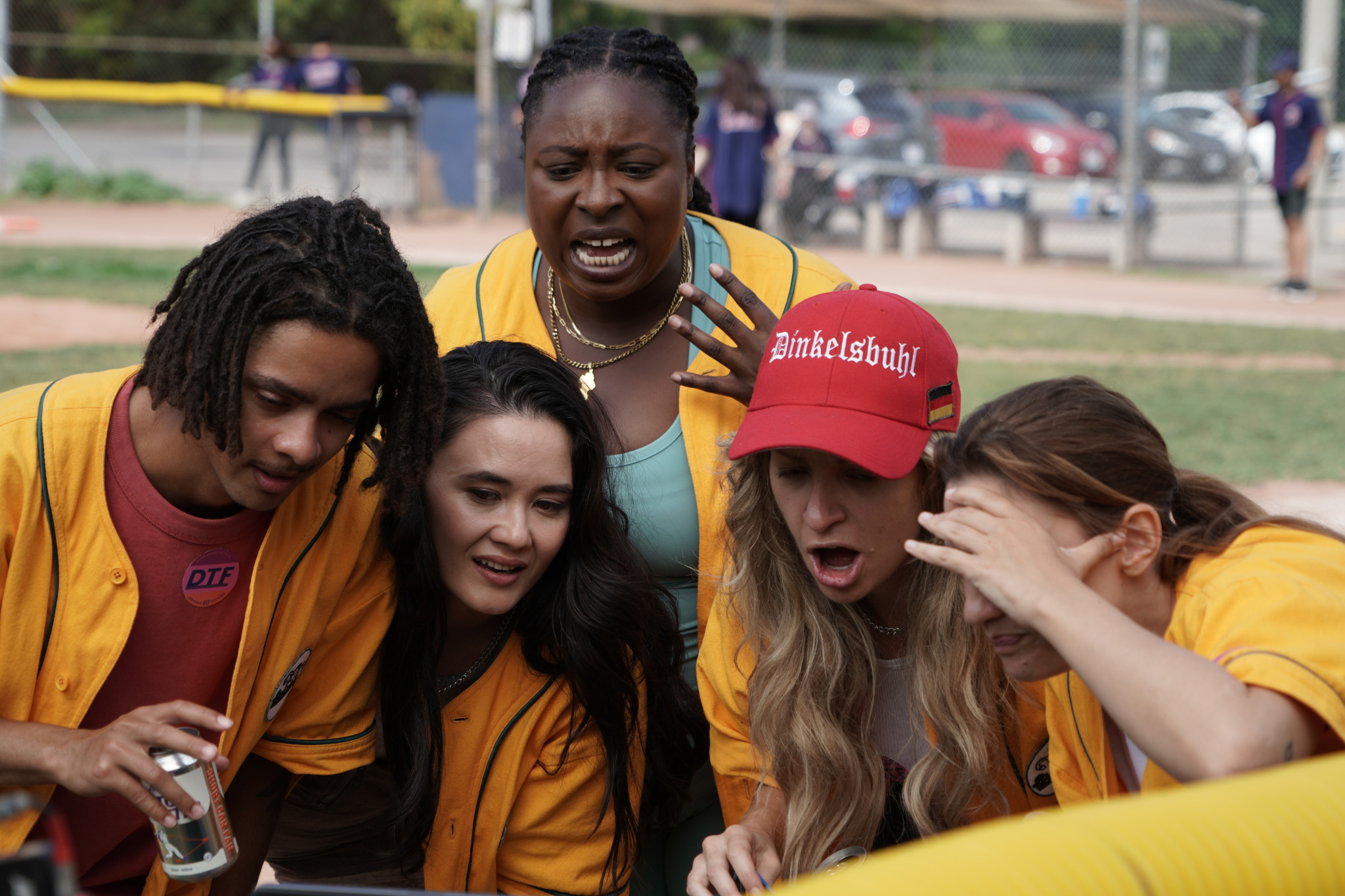 A group of people in yellow baseball uniforms reacts to material on a screen, not seen in the frame, with various expressions of surprise.