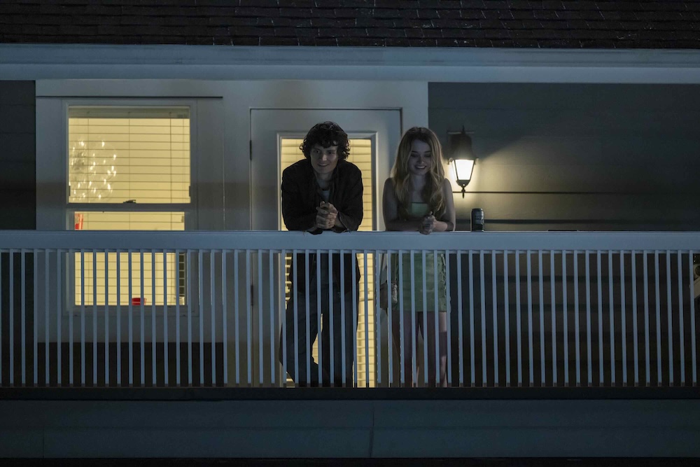 Two actors lean on the white railing of the balcony of a house. At left,  Arthur Conti has short dark hair. At right, Alison Thornton has long wavy blond hair.
