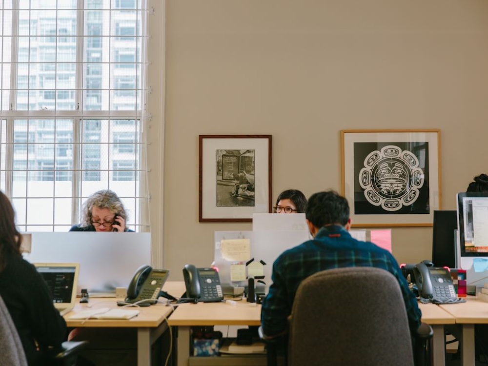 Desks with phones, post-its, laptops and more are occupied by Tyeesters who appear to be working away.