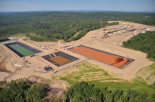 An overhead shot of a fracking site near Fort St. John, featuring three pools of water; two are clay-coloured, one is green.