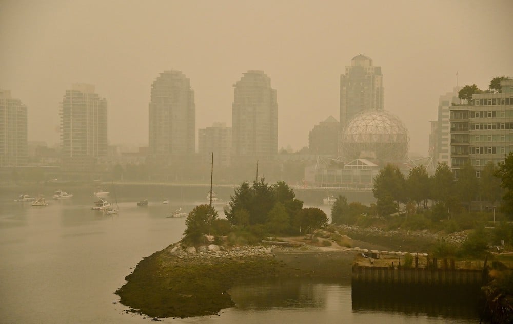 A view looking northeast from the Cambie Street Bridge at False Creek and the buildings around Science World. Heavy wildfire smoke blocks out the mountains and makes Science World barely visible in the orange-brown haze.