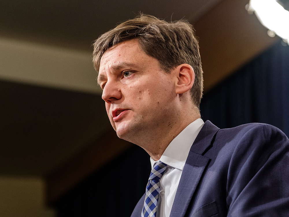 A portrait of David Eby in three-quarters profile. He’s wearing a blue suit with a blue tie, and looks to be listening to someone off-camera.