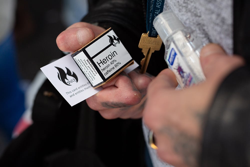 A hand holds a white box labelled ‘Heroin.’