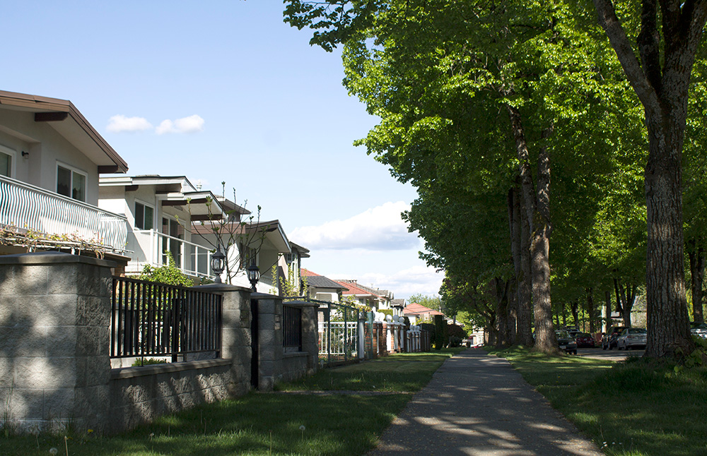 A row of two-storey single-family homes stretches into the distance. There is a sidewalk in front of them, and a broad grassy boulevard with trees.