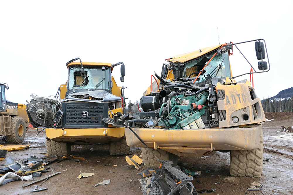 Two large piece of heavy machinery, yellow and black in colour, sit side by side with their windshields smashed and hoods damaged to reveal the engine.