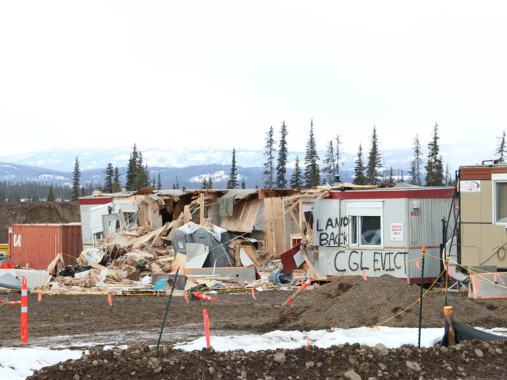 A rural work encampment is trashed and spray painted on a trailer’s outside wall is Land Back.