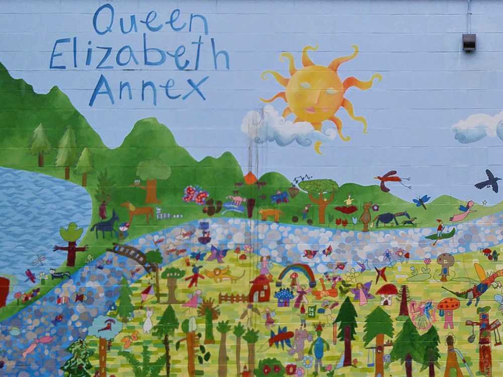 A painted mural including the words “Queen Elizabeth Annex” shows a blue sky, green mountains, a river, a green field, and kids and animals playing.