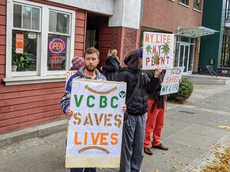 Several people stand in front of a building. They hold signs that say “VCBC Saves Lives” and “VCBC Saved My Life.”