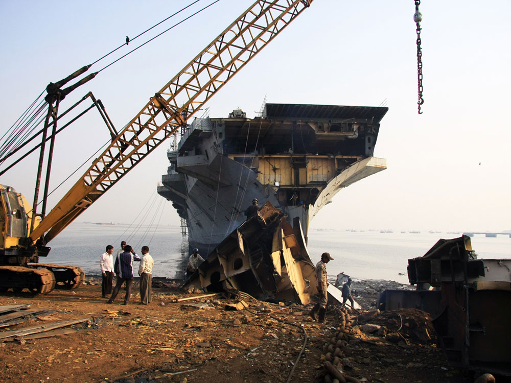 A shipbreaking yard in Darukhan, Mumbai, India. INS Vikrant is being dismantled with scrap metal and workers in background.