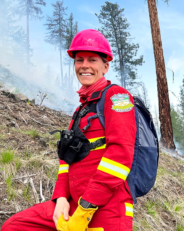 A smiling woman, Kira Hoffman, wearing a bright red work suit and hard hat.