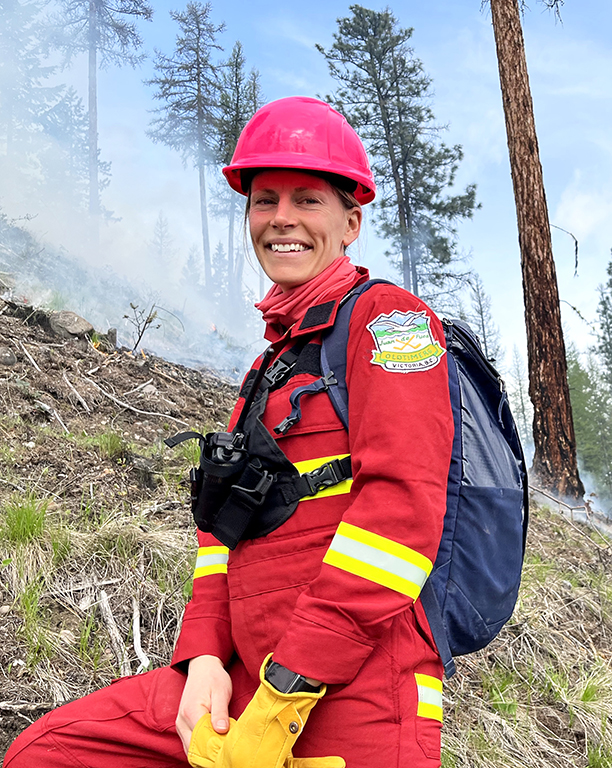 A smiling woman, Kira Hoffman, wearing a bright red work suit and hard hat.