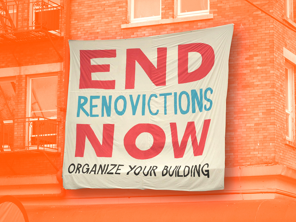 A banner reading “End Renovictions Now. Organize Your Building” is stretched across a brick apartment building.