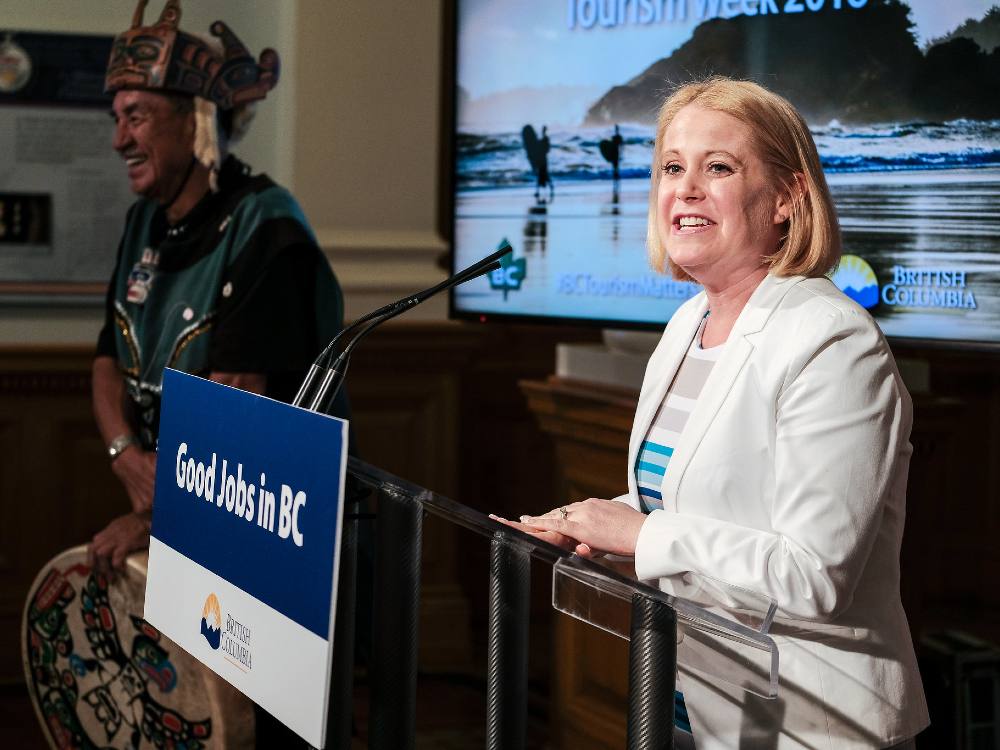 Citizens' Services Minister Lisa Beare stands at a well-lit podium with a sign affixed to it that says "Good Jobs in BC". 