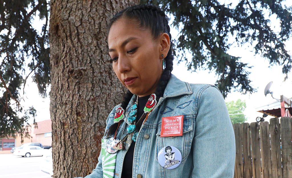 A top photo shows from the air the sprawling Suncor operations, with a road running through that extends towards the Denver downtown skyline. Below this is a photo of Shaina Oliver, dark hair braided and wearing a jean jacket with various buttons including one that say Indigihero. She is looking down, standing next to a pine tree.