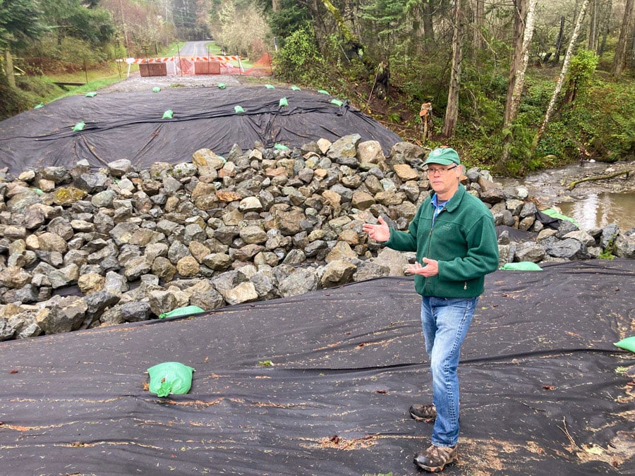 Engineer Calvin VanBuskirk stands on black landscape fabric. A pile of rocks has been placed over the landscape fabric in the mid-section of the picture.