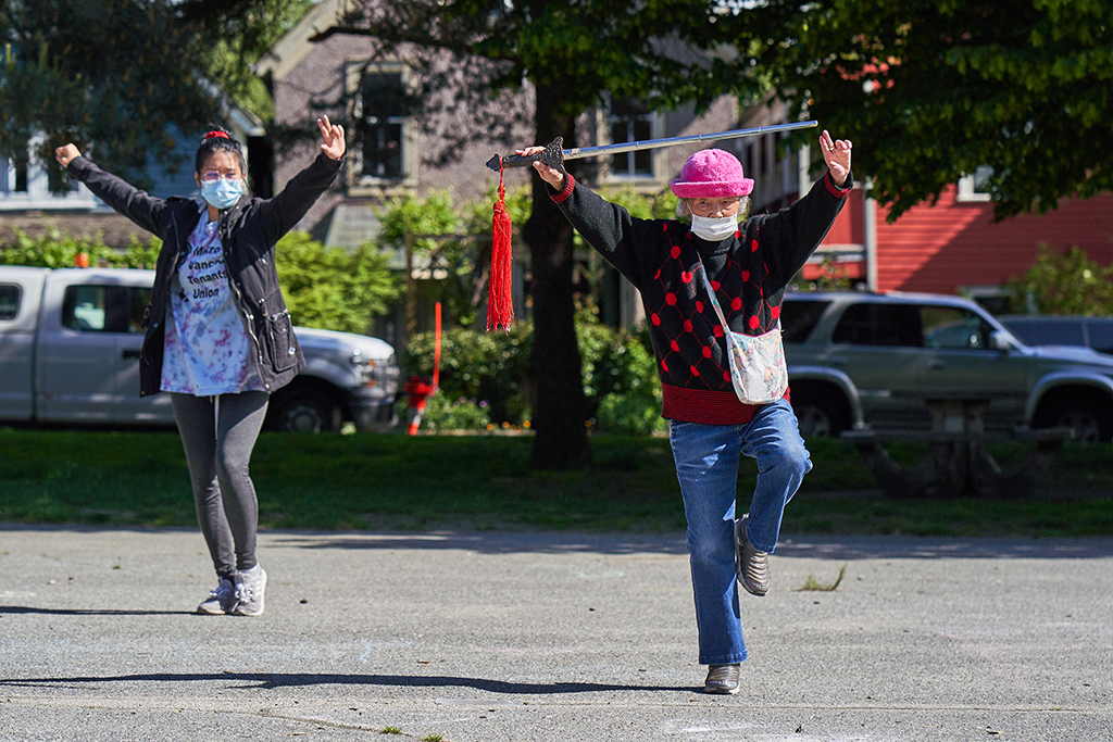 Two people are pictured here practicing tai chi. To the right in the pink hat is Xing Jun Ma, doing a tai chi sword demonstration. Her 27-year-old friend, Beverly Ho (left, in a blue shirt), follows along.