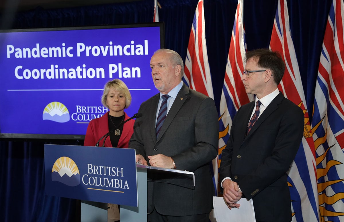 Three middle-aged white people, a blond woman, a bearded man and a clean shaven man, stand before podium with a sign behind them saying Pandemic Provincial Coordination Plan.