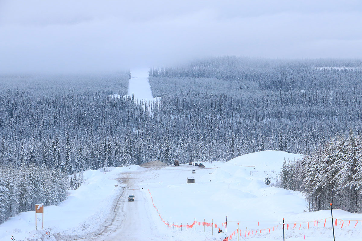 A snowy landscape with forests, some cleared, and a truck parked in the distance.