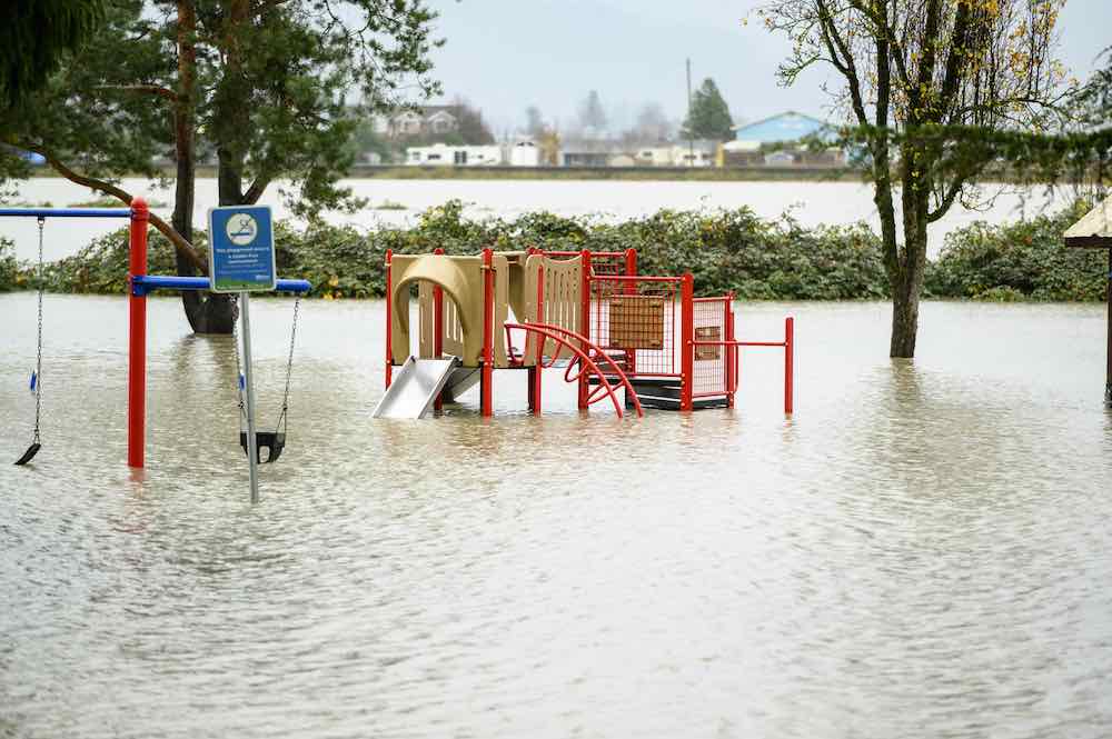 Floodwaters engulf a playground in Abbbotsford, B.C. on Nov. 18, 2021. Red climbing equipment and swings are visible above the water, but we can’t see the ground.