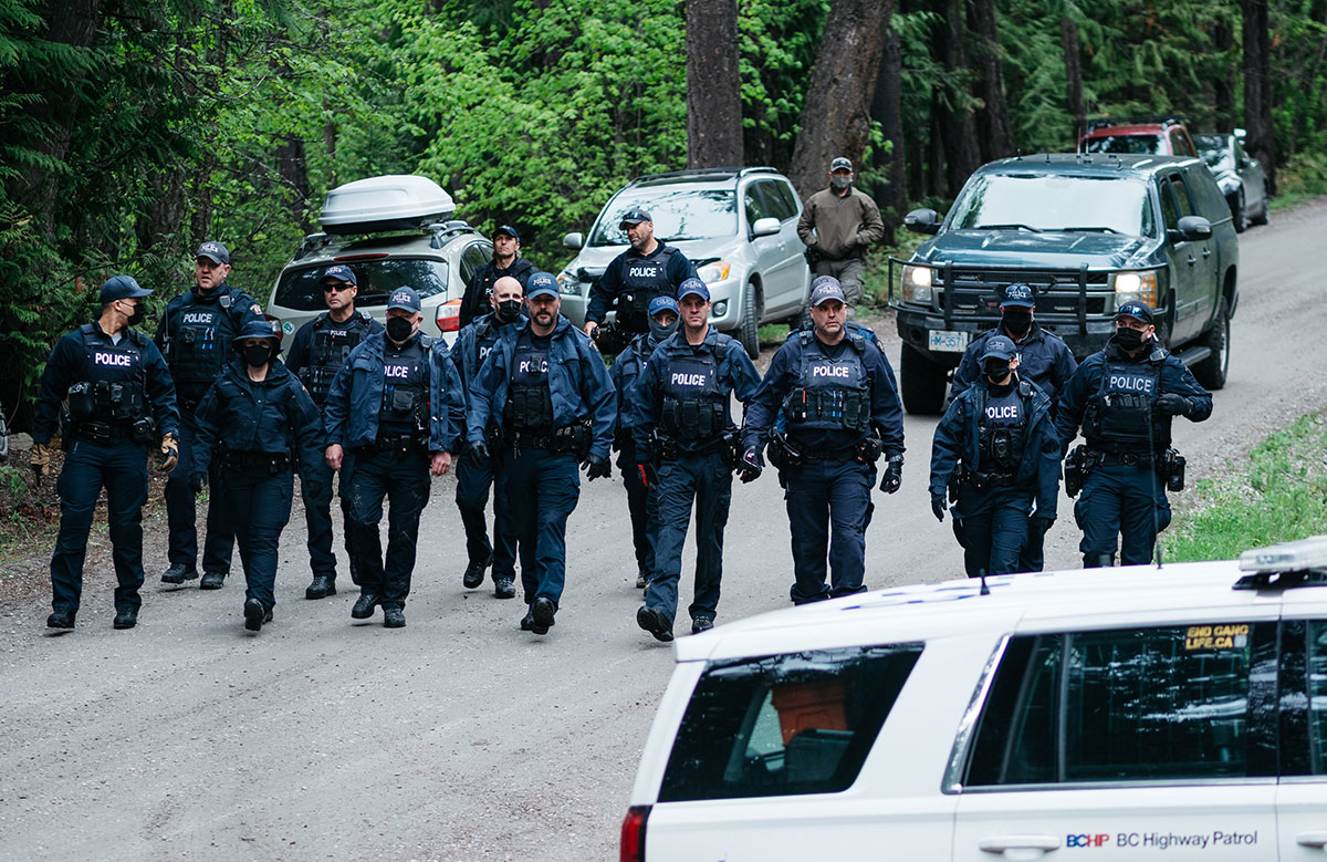 A line of RCMP police officers in dark blue uniforms advances down a logging road.