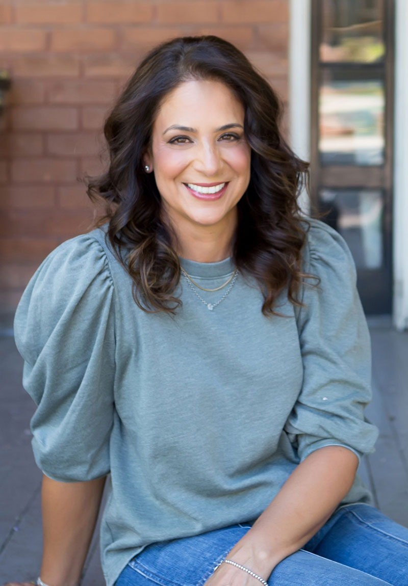 A person with wavy hair, wearing a blue shirt, smiles at the camera.