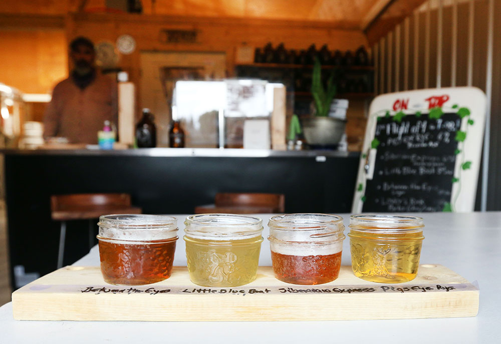 In a cozy, rustic room a tasting flight of four different hued beers sit in mason jars on a wooden slab.