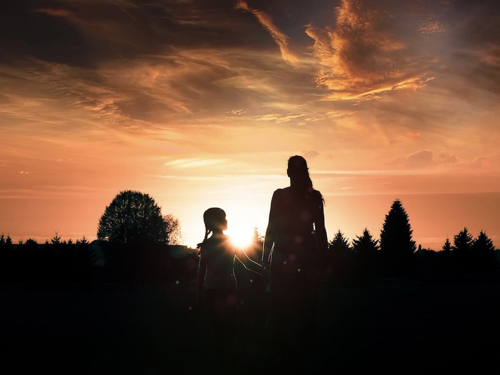 A silhouette of a mother and daughter with a sunset in the backdrop.