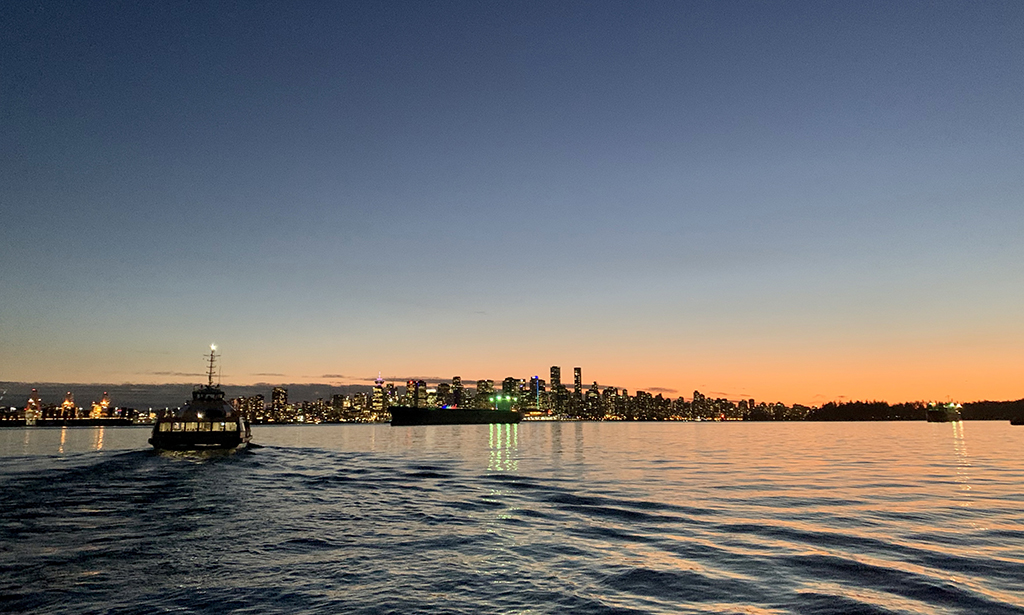 At sunset. The SeaBus heads towards downtown Vancouver, towards darkened buildings with sparkling lights.