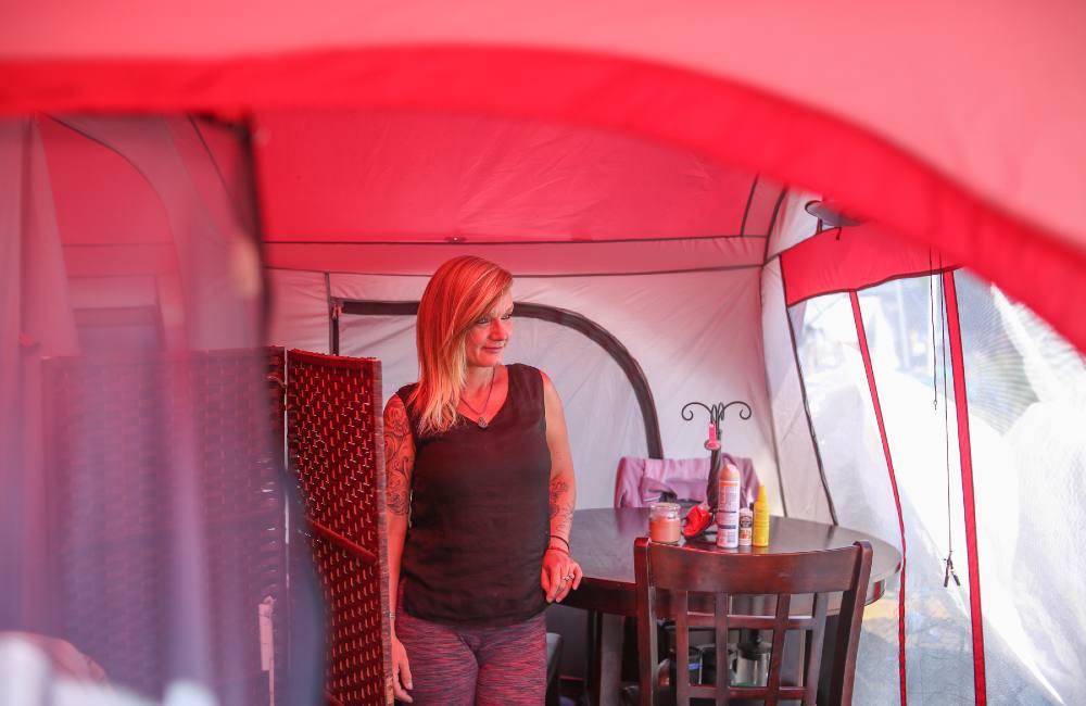 A woman stands inside a clean tent with a couch, carpet, coffee table and dining table.