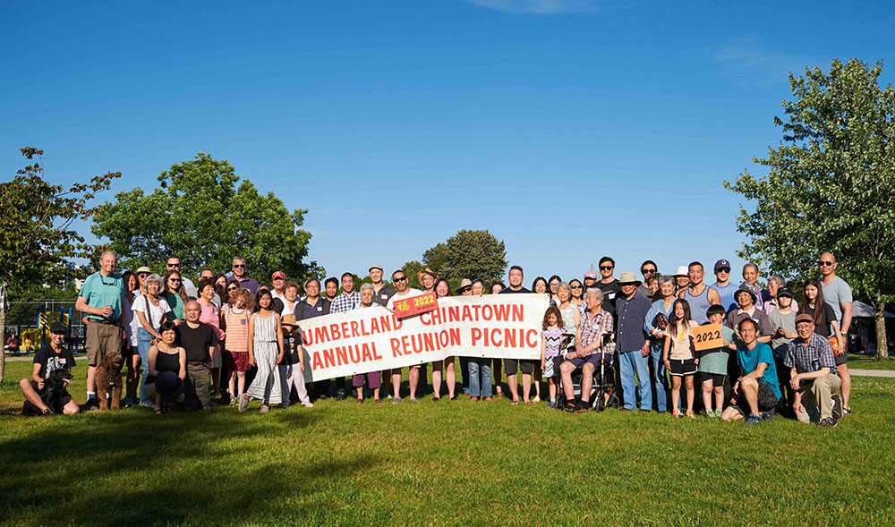 A group photo of the Cumberland Chinatown reunion picnic group on June 26, 2022. They are holding a banner that reads “Cumberland Chinatown Annual Reunion Picnic.”