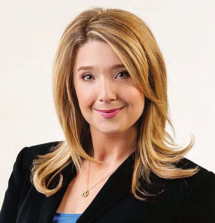 Melissa De Genova has shoulder-length blonde hair and is wearing a black blazer. She is seated against a white studio background.