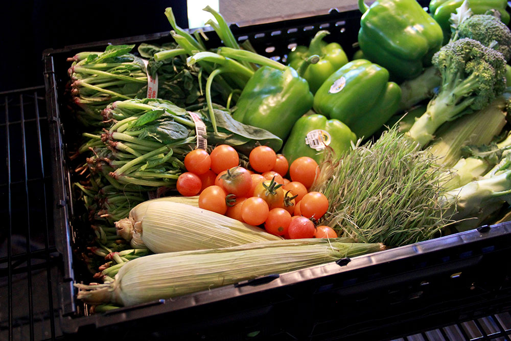 A produce box containing corn, spinach, peppers, tomatoes and broccoli.