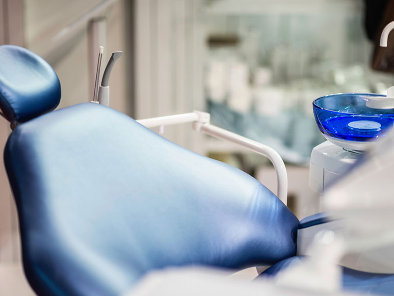 An empty dentist chair in recline is surrounded by instruments.