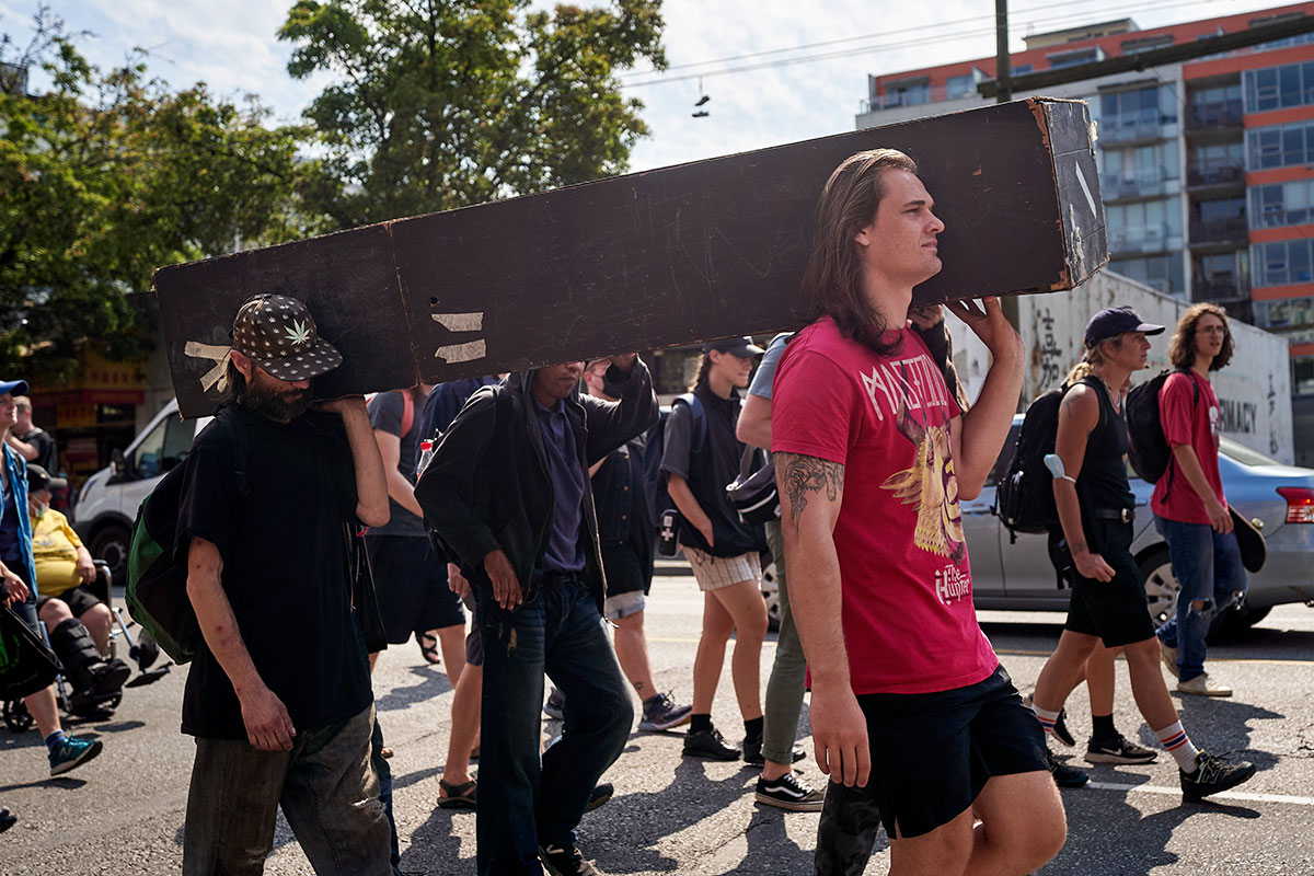 In the middle of a march, people carry a black-painted wooden coffin down the street.