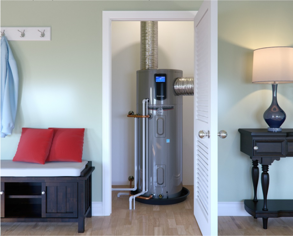 A silver electric heat pump water heater sits in the closet of a tidy home with green walls. 