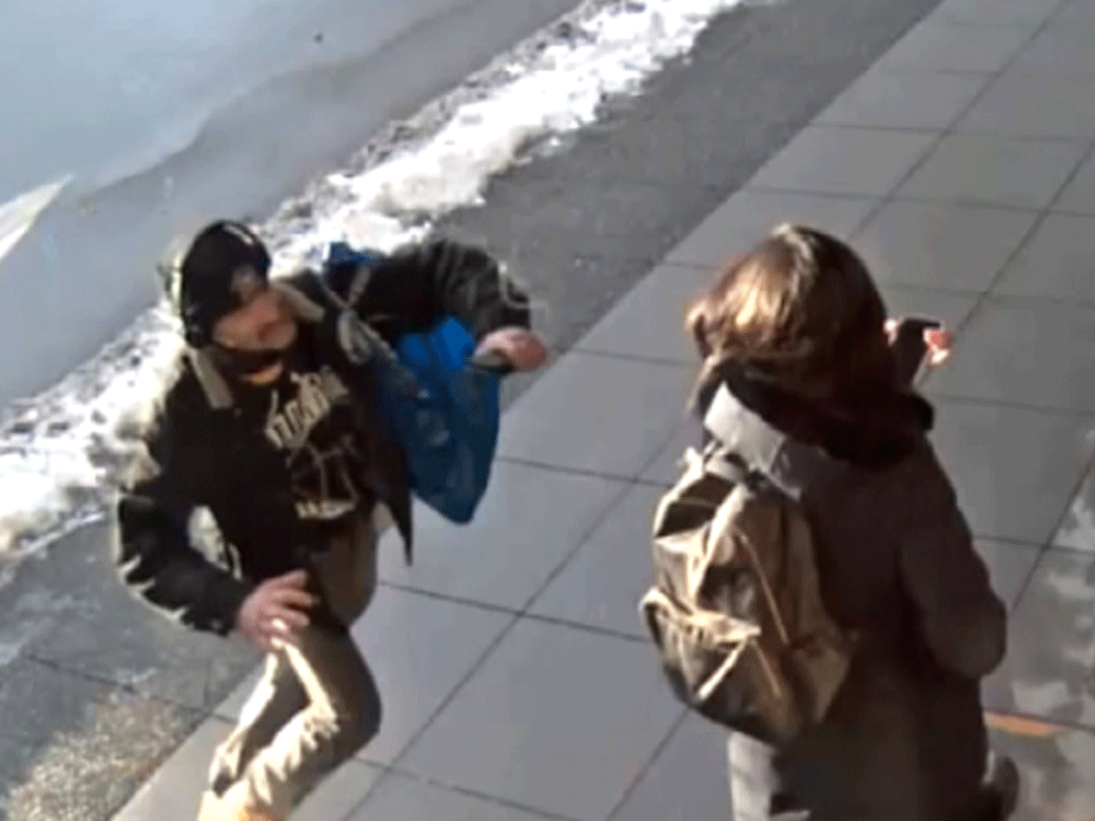 A frame from security footage of a downtown street showing a man suddenly lunging at a woman.