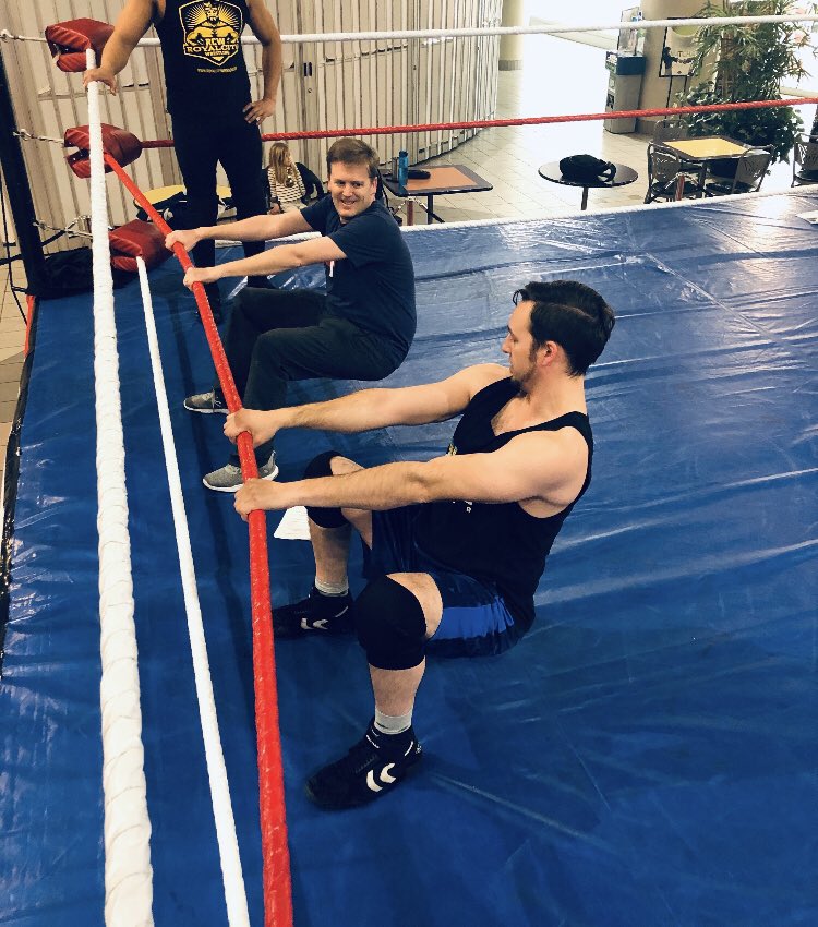 A wrestling ring with two men holding onto the ropes and leaning back.