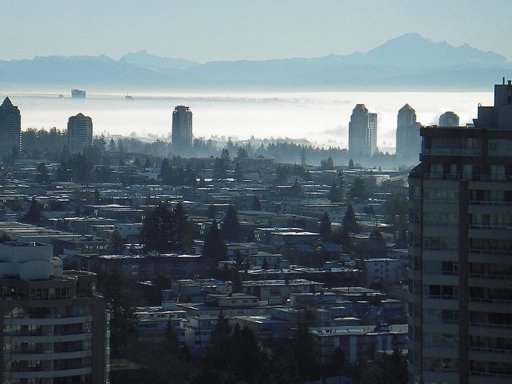 Mount Baker rises in the hazy distance, from a vantage overlooking the rooftops of Surrey, a handful of towers poking up, and a stripe of fog beyond.