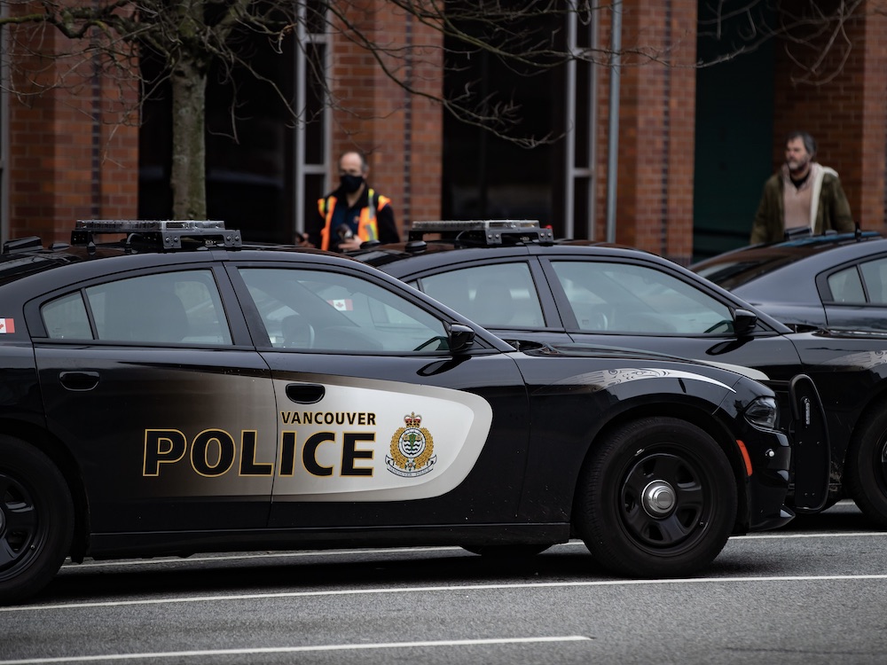 A row of black-and-white Vancouver police department vehicles with a police officer out of focus behind.