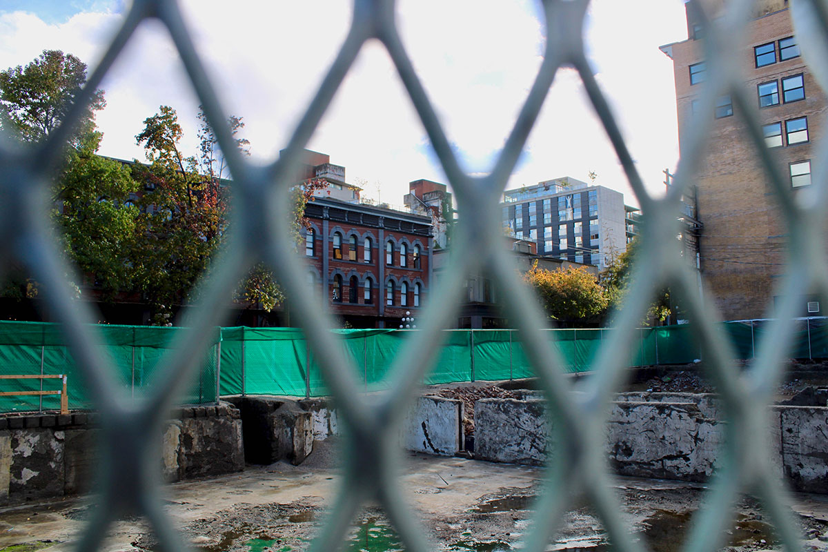 A photo taken through a chai link fence shows the cleaned-up basement of the Winters Hotel, destroyed by fire and demolished in April. Solid green fencing blocks the back of the site.