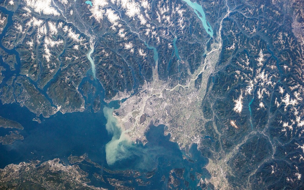 An aerial photo of the Fraser estuary, which shows coastal mountains, the ocean and much human development.  